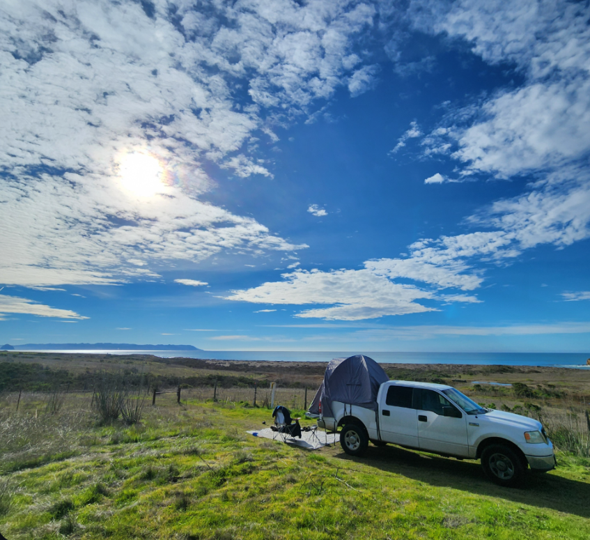 A truck and tent at a coastal campsite beneath a wide evening sky